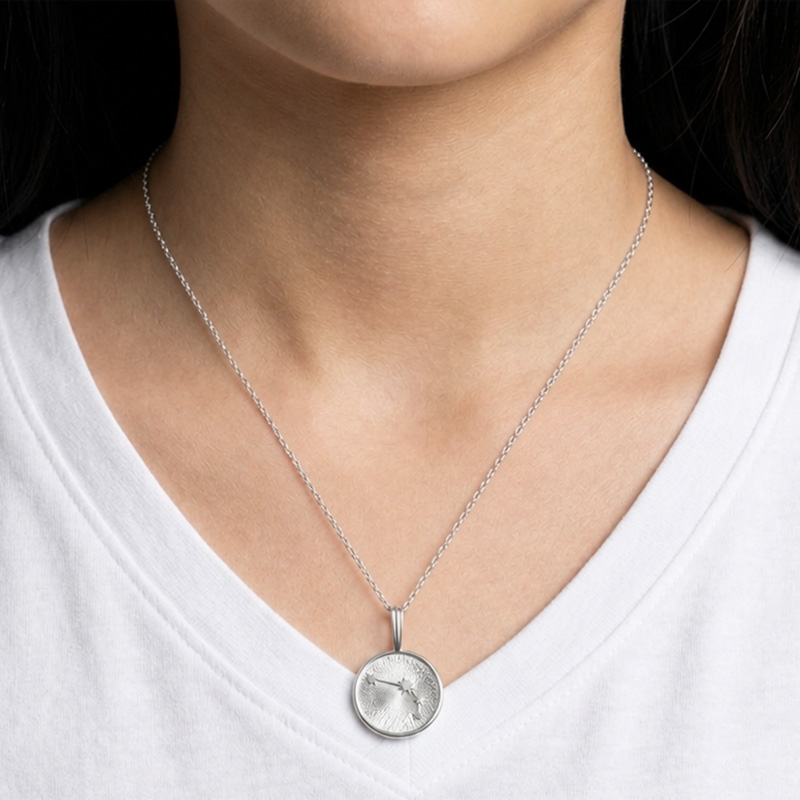 Silver circular pendant necklace on a delicate chain resting at the chest over a white V-neck shirt