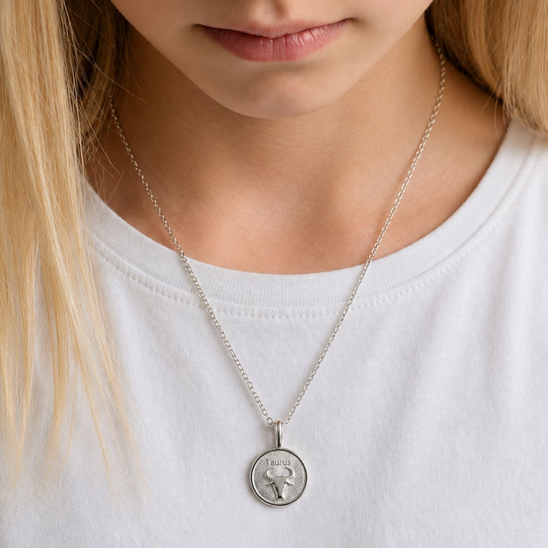 Close-up of a silver Taurus pendant necklace resting on a white T-shirt, worn by a person with blonde hair.